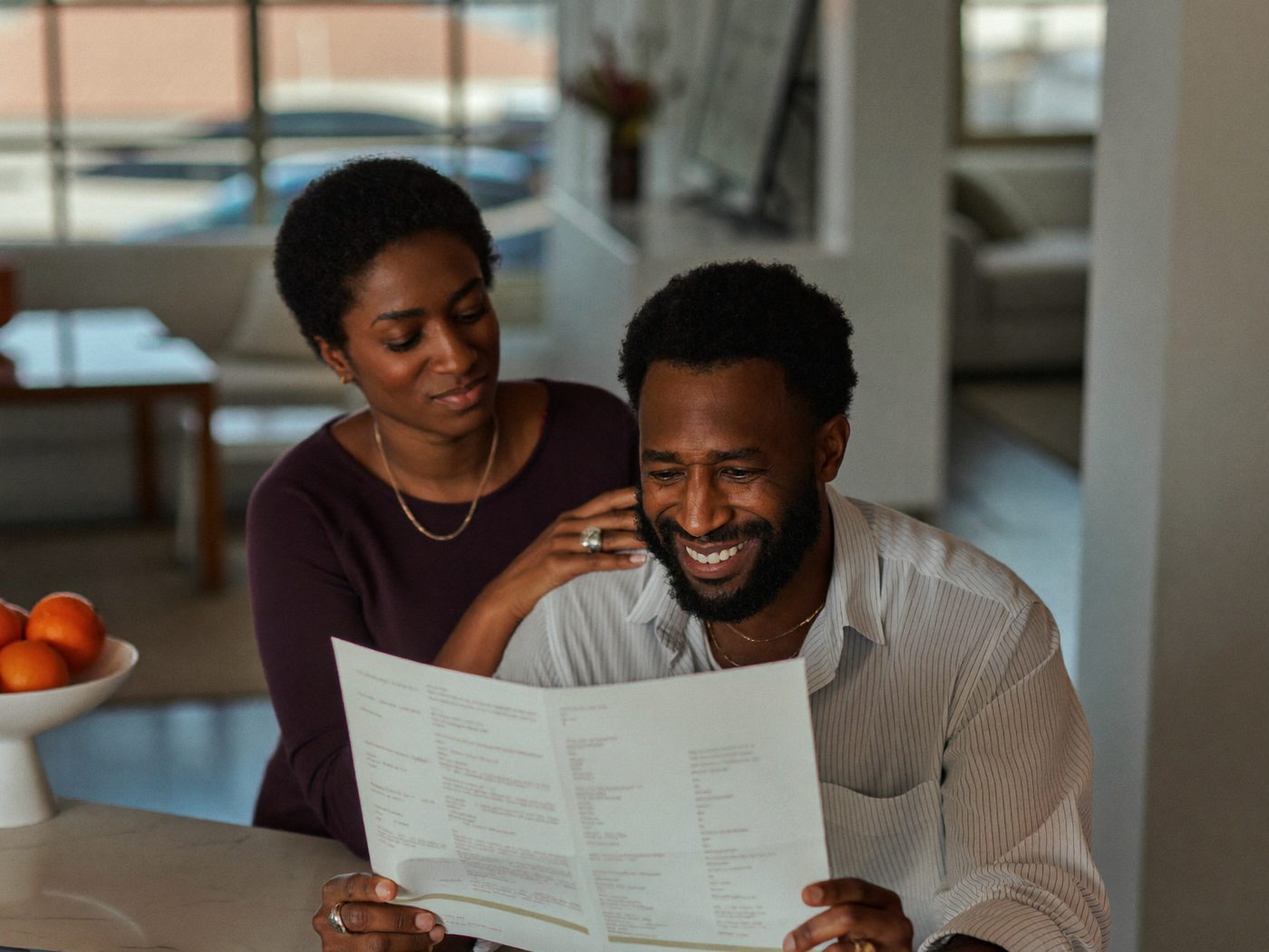A man reading his Signal report on his phone at the kitchen counter, his wife's hand on his shoulder